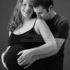 Black and white maternity portrait of man in black t-shirt kissing the shoulder of wife in black camisole